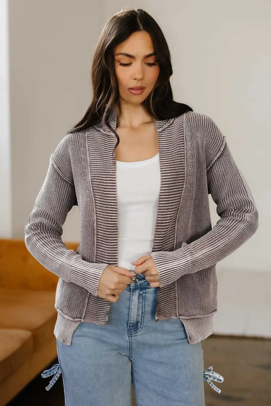 Front view of model adjusting brown Women's Stonewash Patchwork Knit Open Cardigan, paired with white tank and jeans.