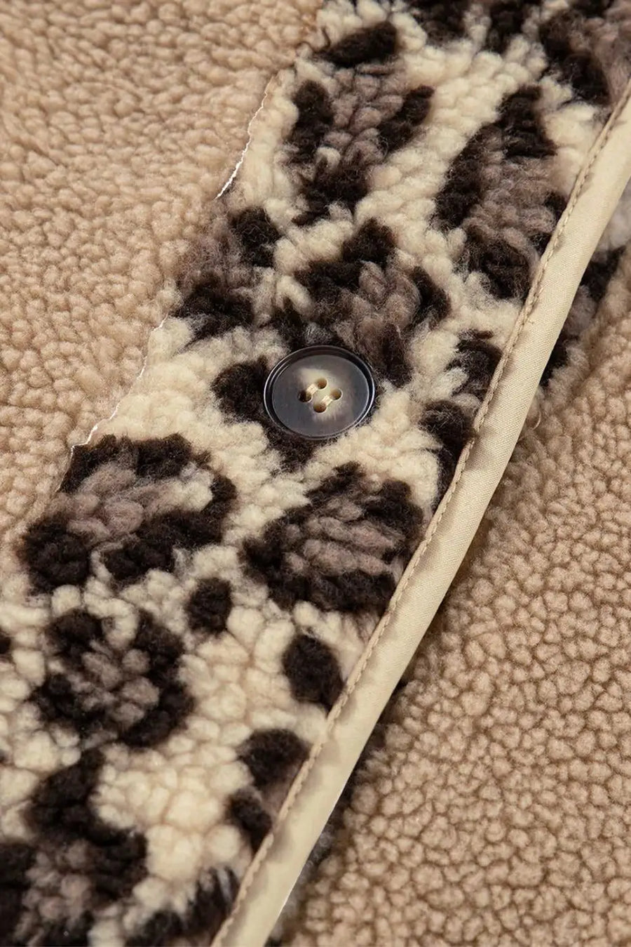 Macro shot of button and leopard print fleece fabric on women’s plush jacket, emphasizing texture and stitching detail.