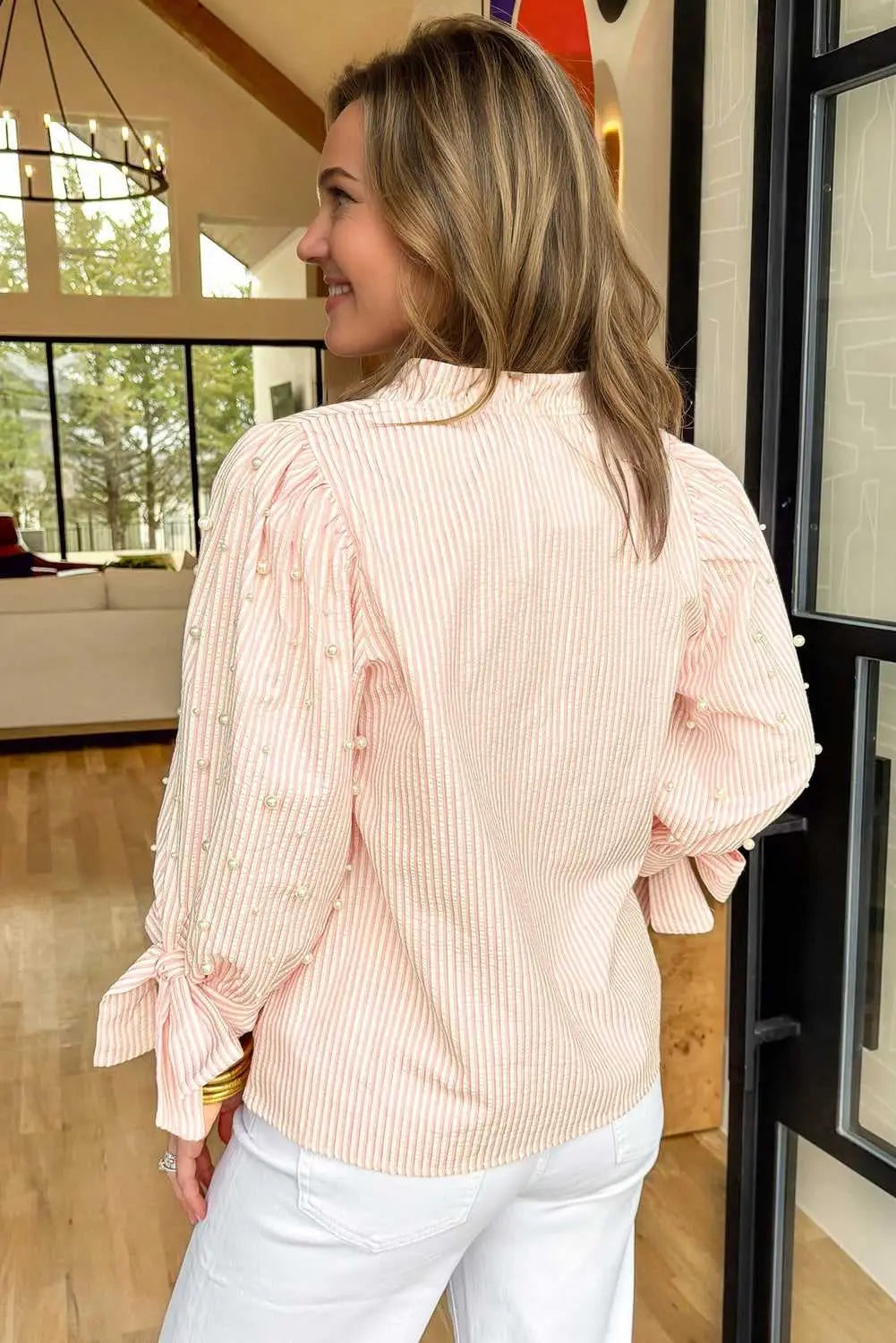 Back view of the Bow Cuff Pearl Embellished Blouse worn by model, featuring pearl-detailed sleeves and bow cuffs.