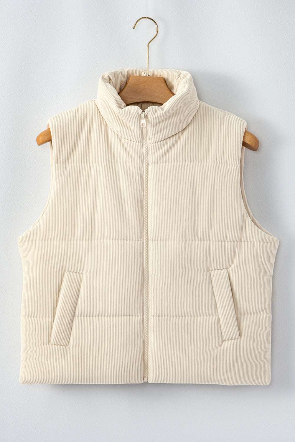 Beige corduroy puffer gilet with stand neck and zipper, displayed on hanger to highlight quilted texture and front pockets.