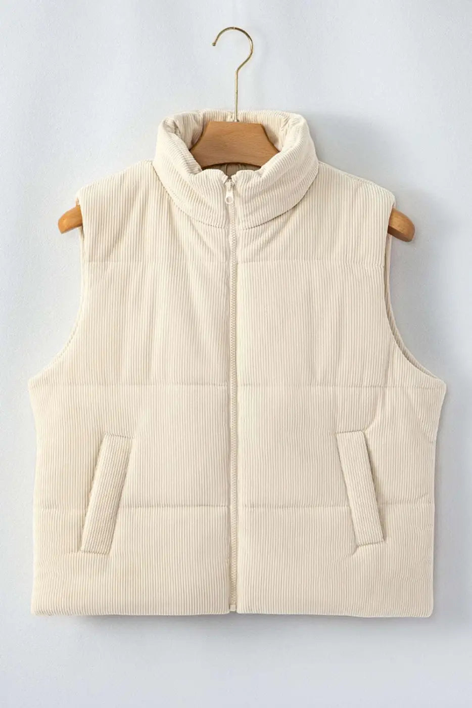 Beige corduroy puffer gilet with stand neck and zipper, displayed on hanger to highlight quilted texture and front pockets.