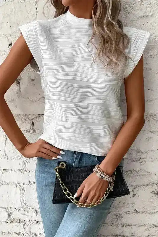 Textured white mock neck top with cap sleeves and fitted silhouette, styled with jeans and accessories for a modern look.