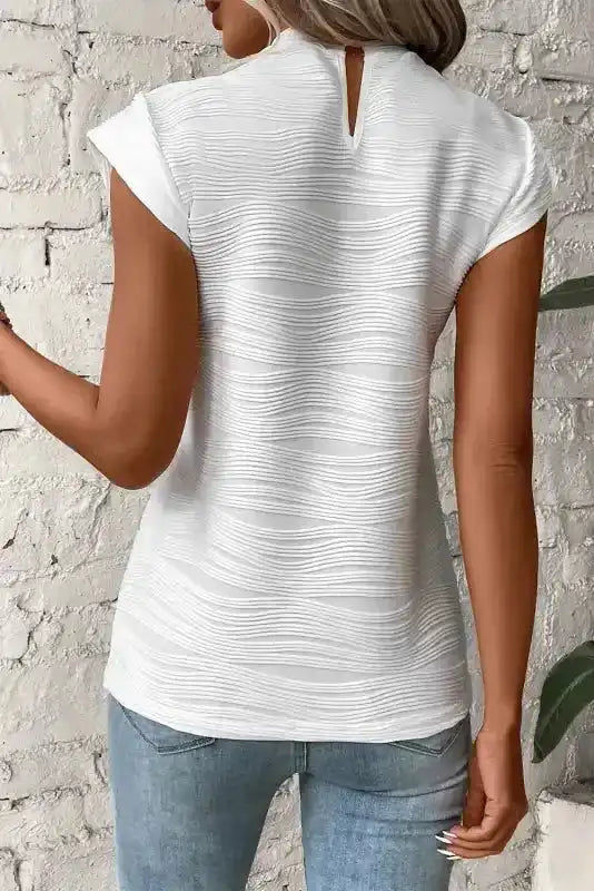 Back view of white textured cap sleeve mock neck top featuring a keyhole closure, paired with light blue jeans for daily wear.