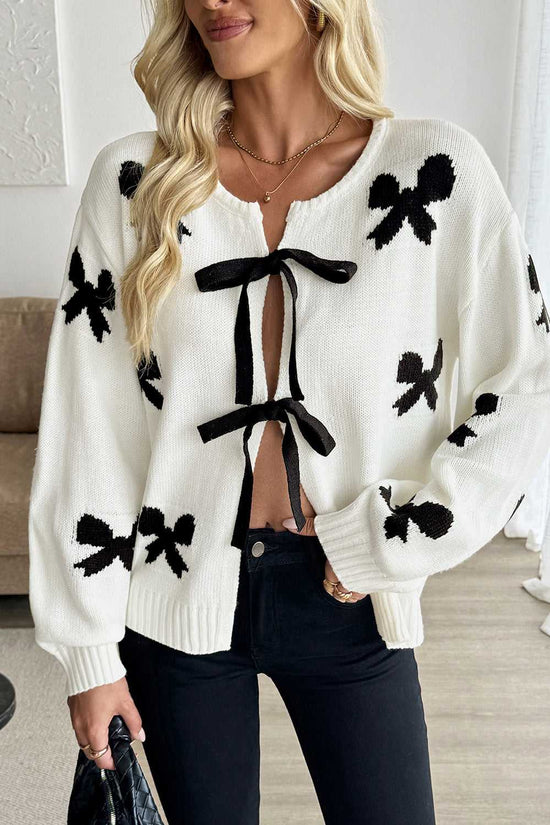 Romantic White Bow‑Lace Knit Cardigan with black bow prints and front tie closure, styled with black jeans for a feminine casual look.