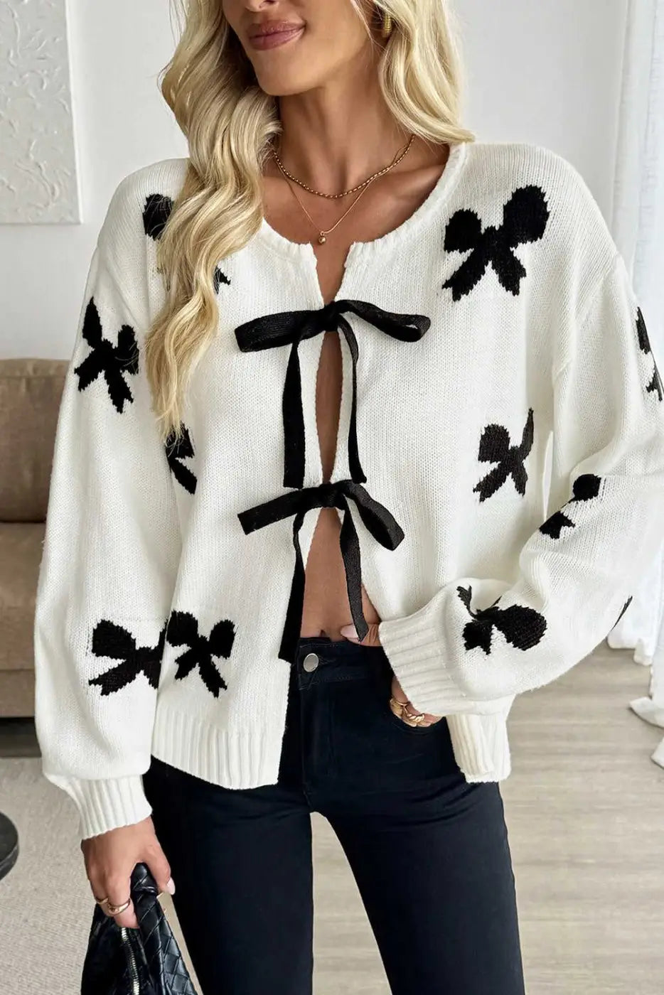 Romantic White Bow‑Lace Knit Cardigan with black bow prints and front tie closure, styled with black jeans for a feminine casual look.