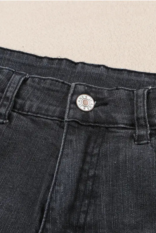 Close-up of dark denim jeans waistband with metal button on distressed ripped denim shorts