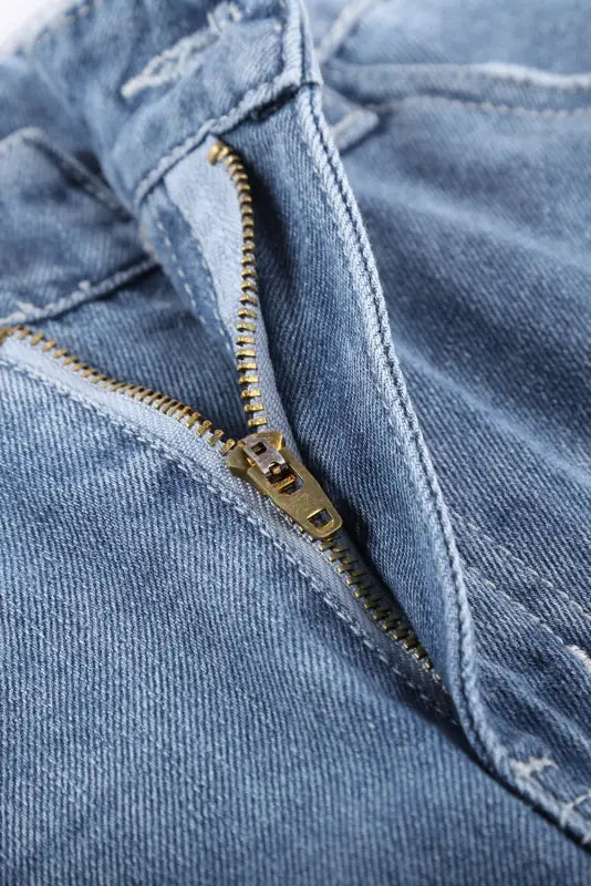 Close-up of zipper on distressed ripped denim shorts - rolled hem in light blue denim