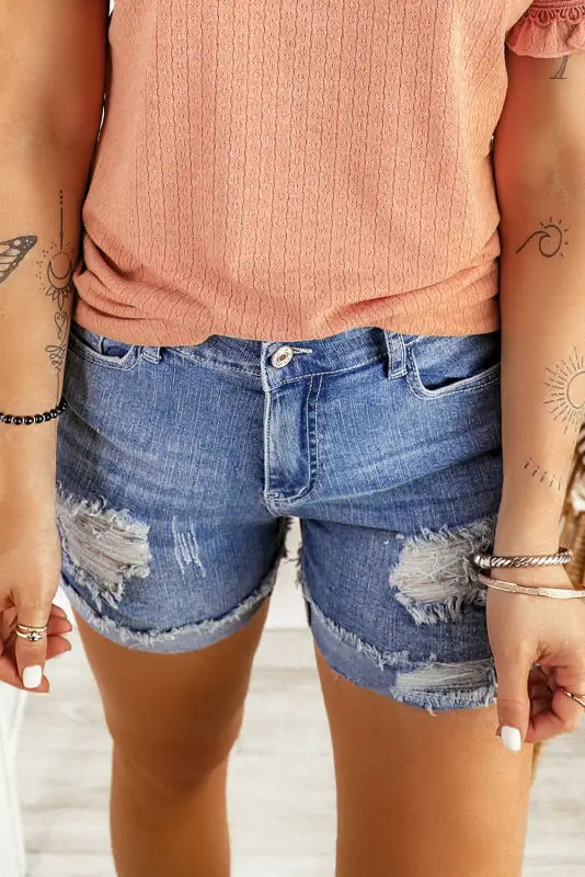 Distressed ripped denim shorts with rips, frayed edges, and rolled hem for a relaxed look