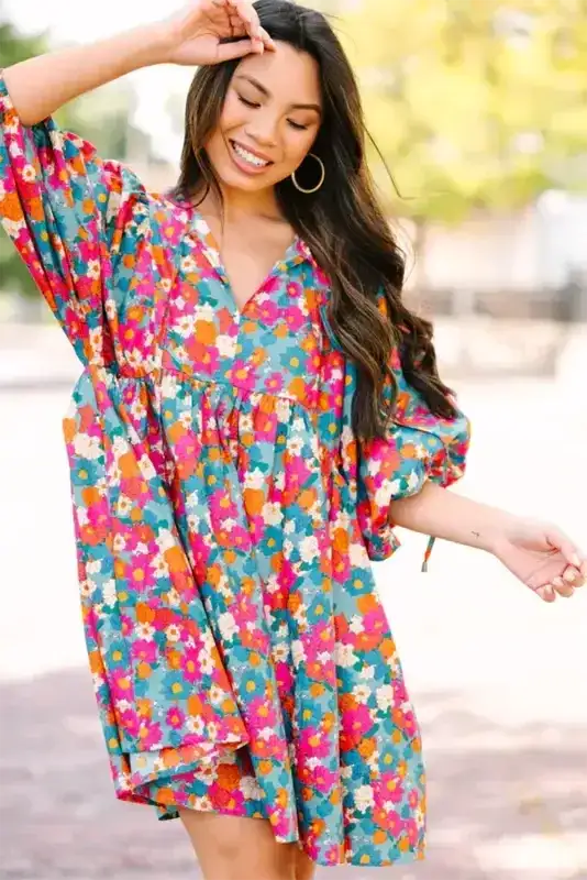 Close-up of woman wearing a sky blue floral babydoll dress with tie neckline and voluminous bubble sleeves in a cheerful floral pattern.