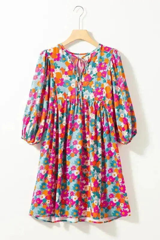 Sky blue floral babydoll dress with tie neckline and bubble sleeves displayed on hanger, highlighting its colorful summer print.