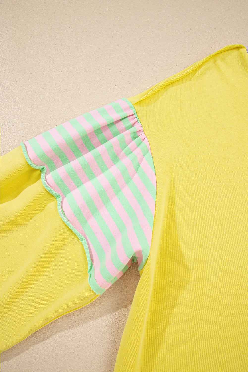 Detail view of striped sleeve on plus size yellow sweatshirt, featuring pink and green stripes with scalloped stitching.