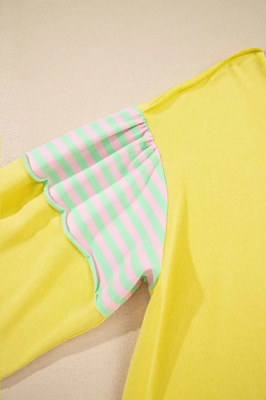 Detail view of striped sleeve on plus size yellow sweatshirt, featuring pink and green stripes with scalloped stitching.
