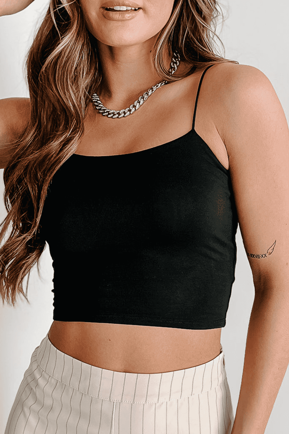 Black spaghetti strap skinny fit crop top with stretch fabric, styled with beige pinstripe pants for a sleek summer outfit.