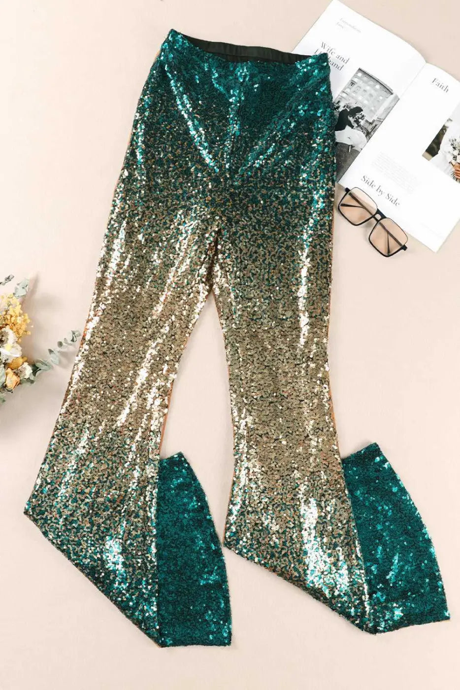 Flat lay of green sequin flared trousers with gold gradient. Sparkly party pants with flared legs, ideal for festive occasions.