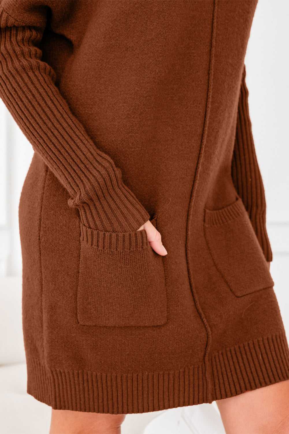 Close-up of pocket and ribbed sleeve detail on brown knit jumper dress. Cozy and stylish women’s winter sweater dress in solid color.