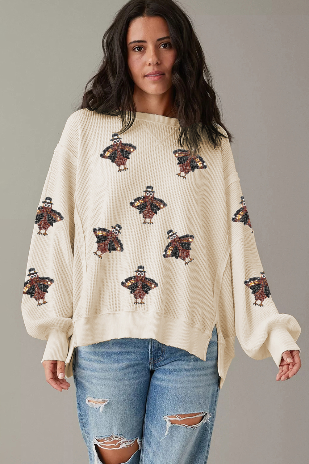 Woman wearing a cream sweater with teddy bear patterns and blue jeans on a gray background