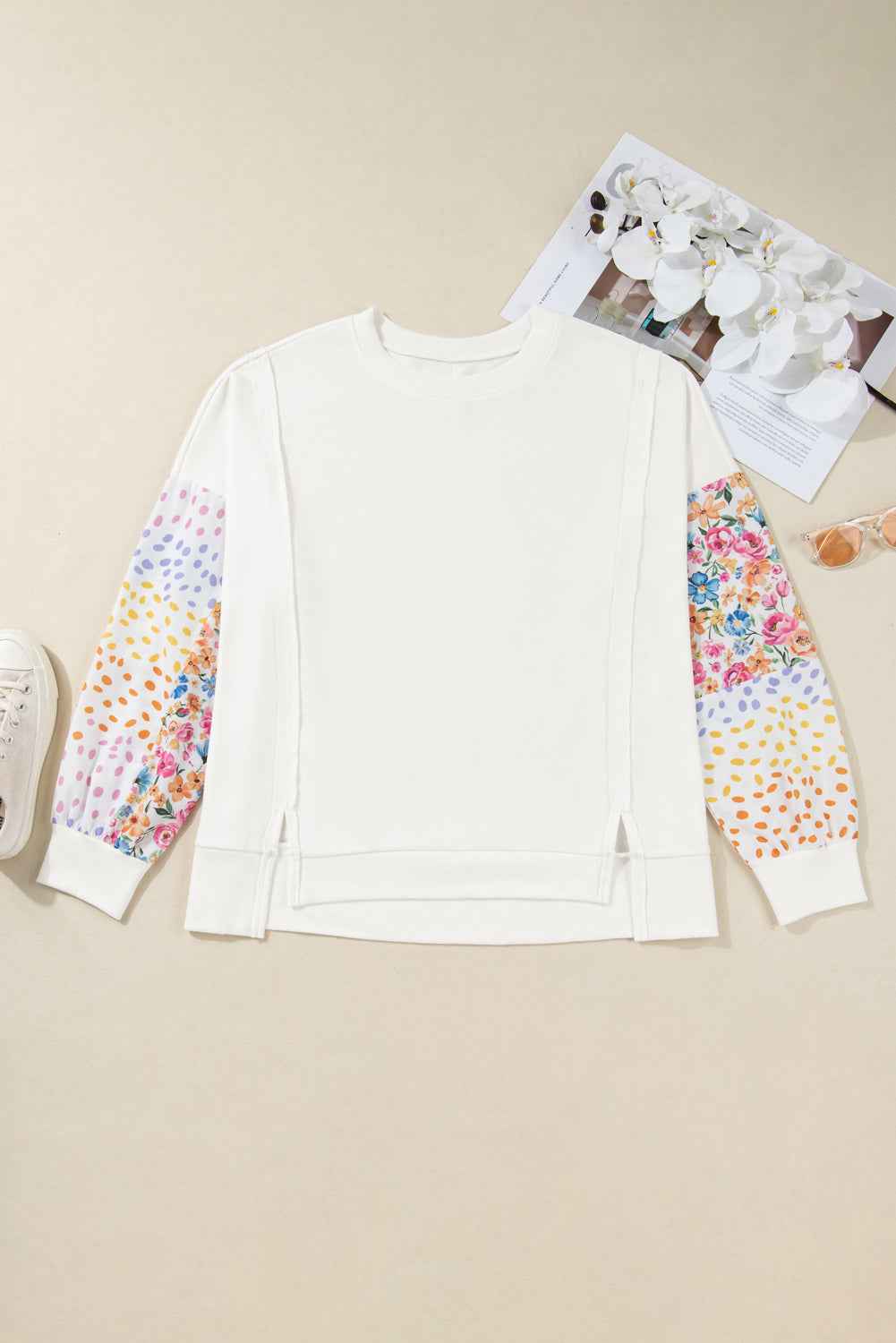 Flat lay of plus size floral sleeve sweatshirt with colorful patchwork sleeves. Features side slits and soft fabric for daily comfort.