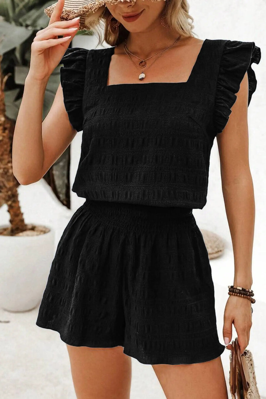 Woman wearing a black top and shorts set with ruffled sleeves, standing outdoors.