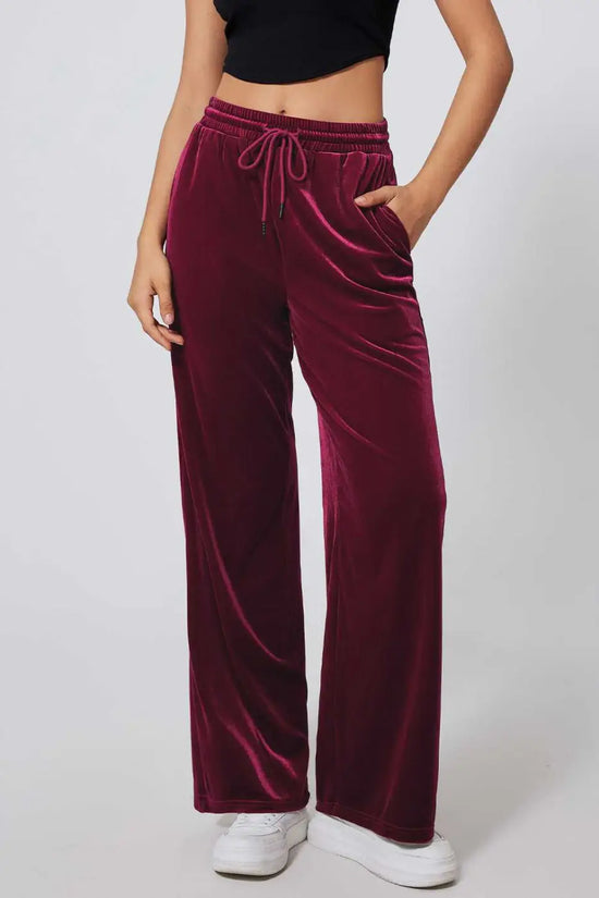 Burgundy velvet drawstring trousers with wide-leg silhouette, styled with a black crop top and white sneakers for casual activewear.