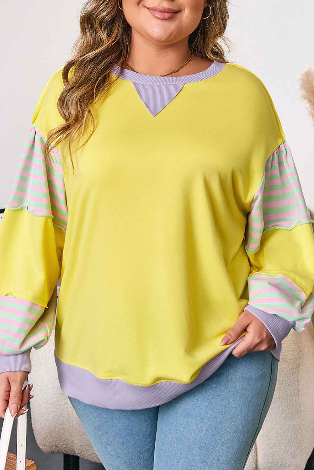 Close-up of plus size yellow sweatshirt highlighting lilac neckline and striped sleeve design for a stylish casual look.