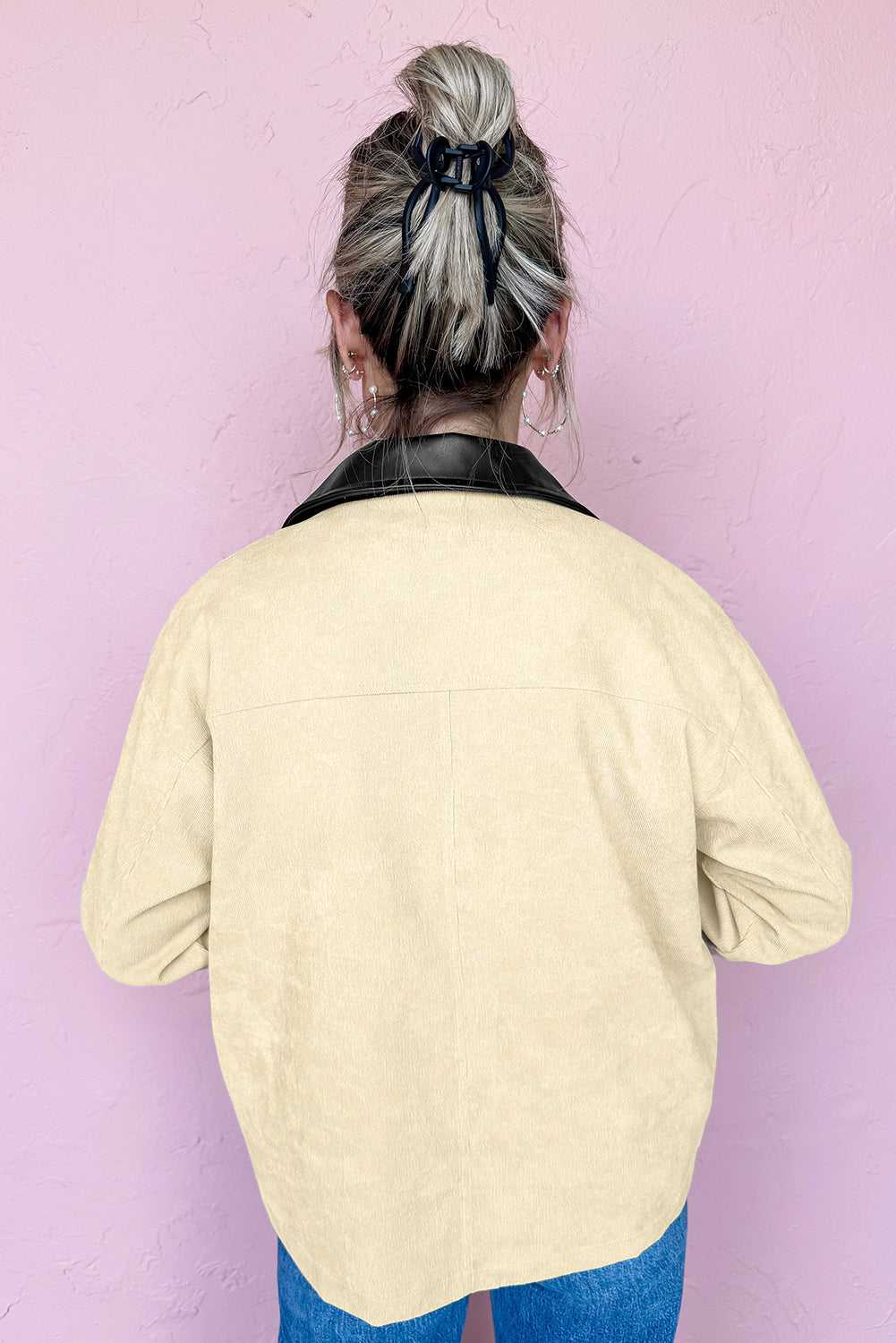 Person wearing a light yellow jacket with a black collar against a pink wall
