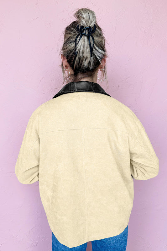 Person wearing a light yellow jacket with a black collar against a pink wall