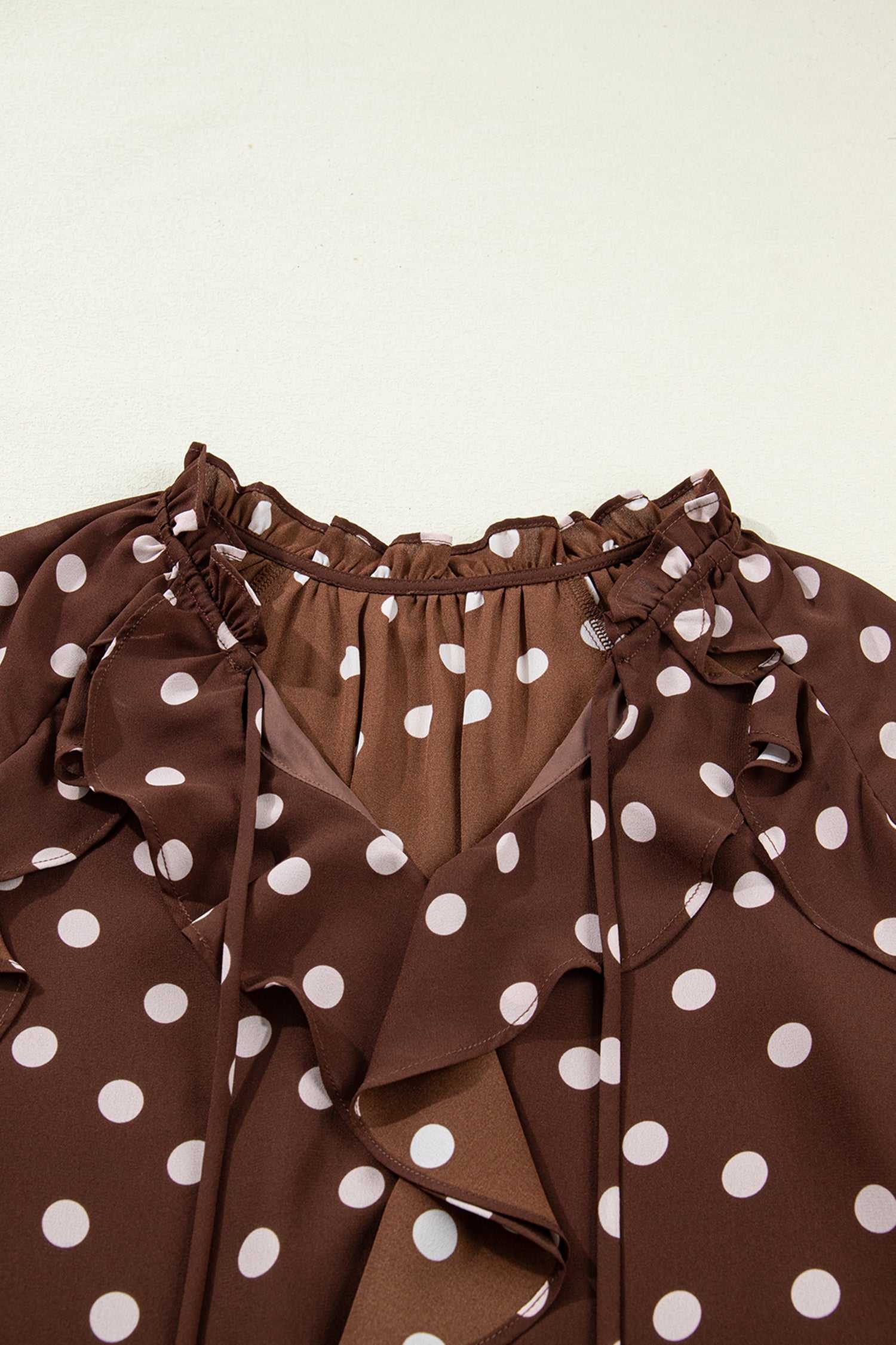 Close-up of the neckline on the coffee polka dot bell sleeve blouse, featuring a chiffon tie neck and soft ruffle trim for a feminine touch.