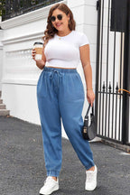 Model wearing Plus Size Blue Denim Joggers with white crop top and sneakers, showcasing a trendy and comfortable streetwear look.