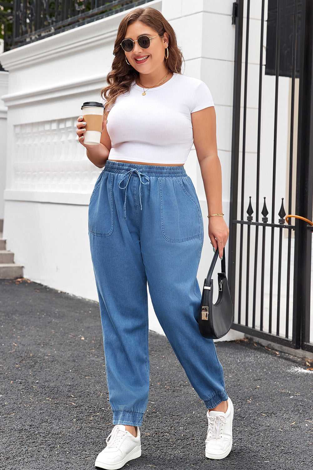 Model wearing Plus Size Blue Denim Joggers with white crop top and sneakers, showcasing a trendy and comfortable streetwear look.