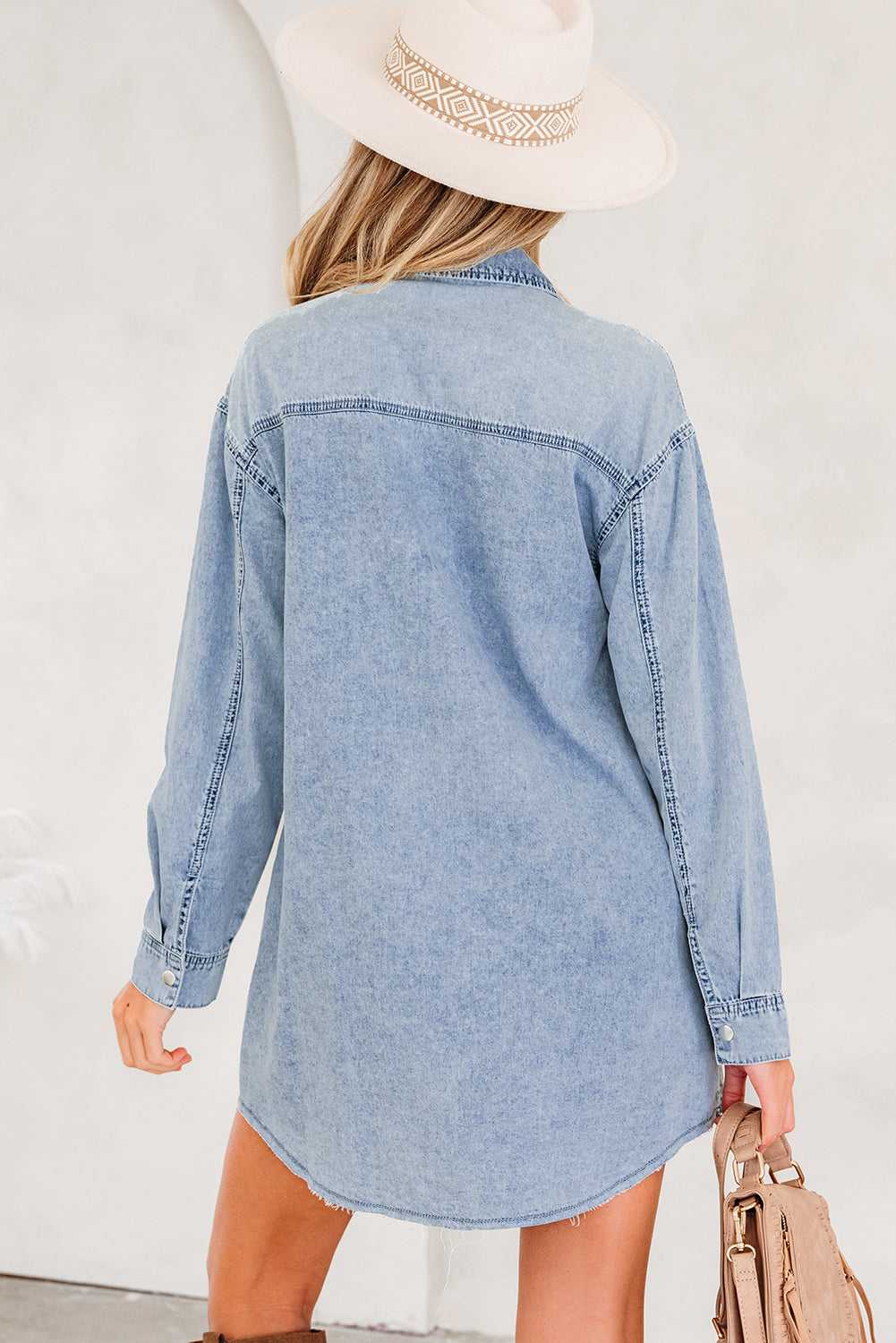 Back view of light blue oversized denim shirt dress with curved hem and relaxed fit, ideal for casual fall and autumn fashion.