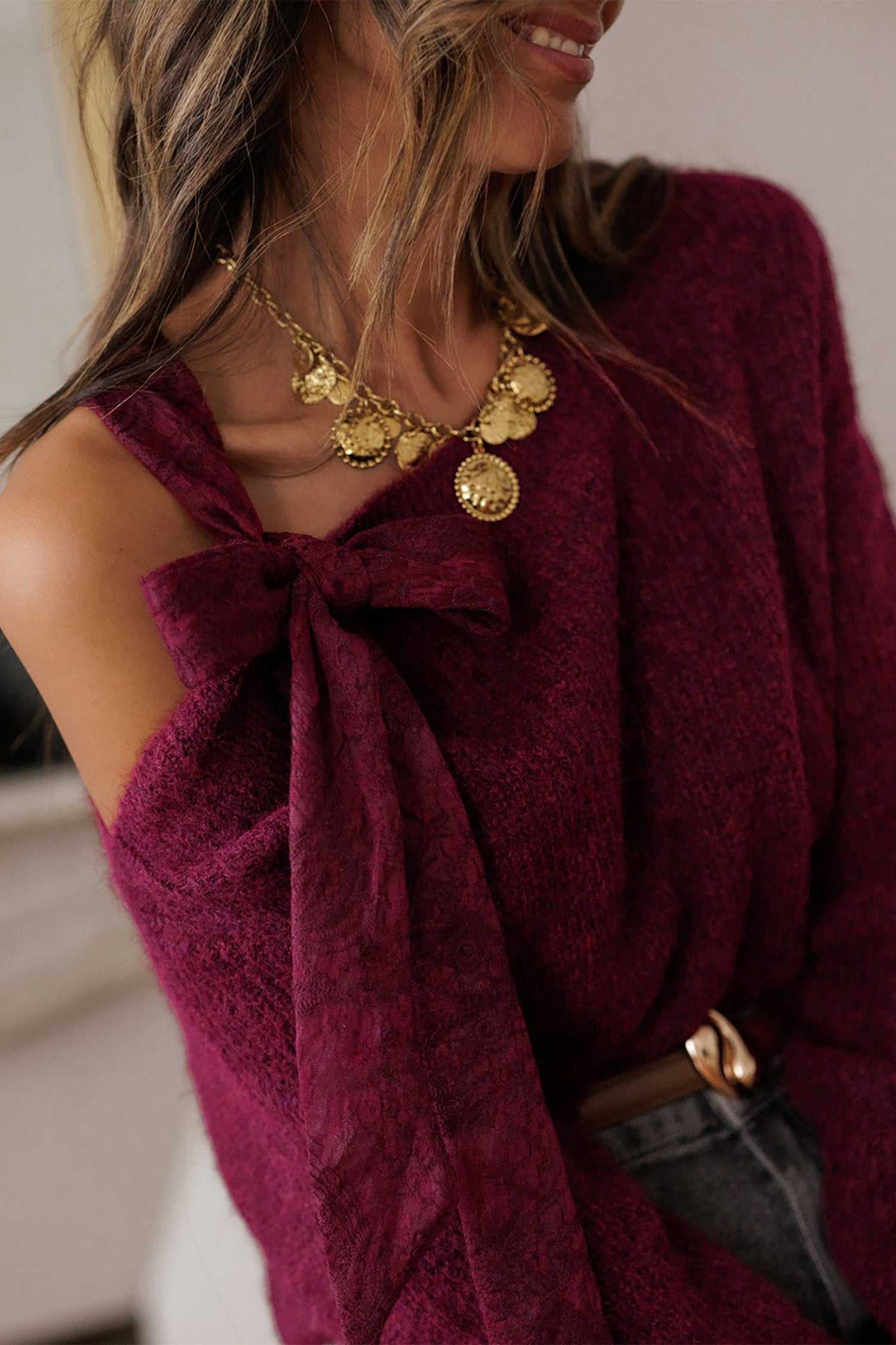Close-up of burgundy off-shoulder sweater with lace bow and soft knit texture. Elegant fall top for women, perfect for layering and accessorizing.