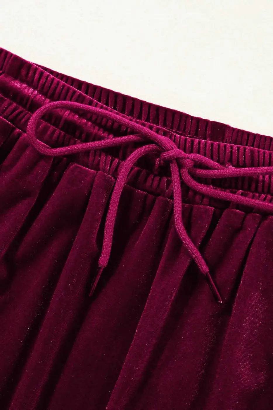 Close-up of drawstring waistband on burgundy velvet trousers, highlighting soft fabric and adjustable fit for activewear comfort.