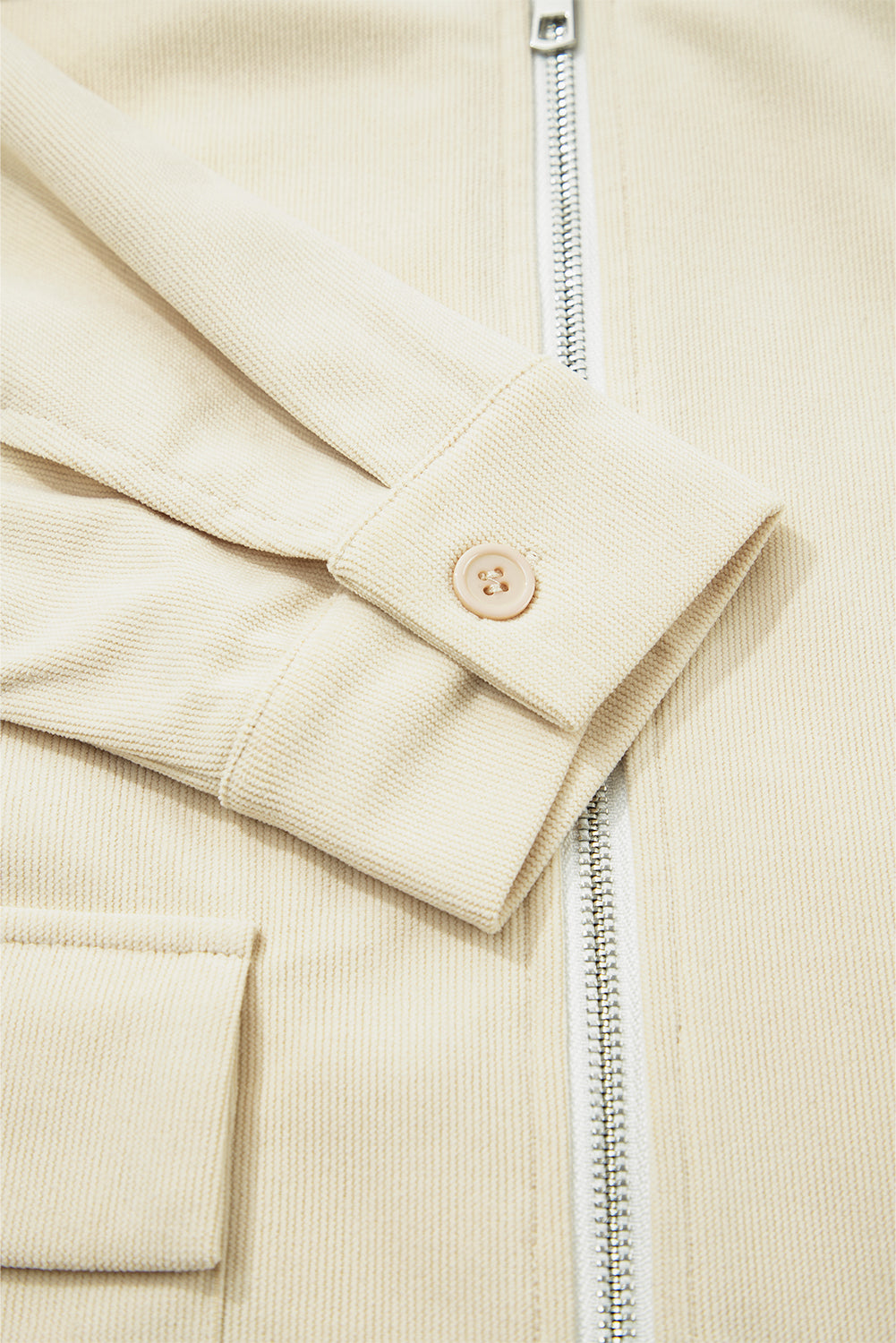 Close-up of a beige corduroy jacket with a zipper and button detail.