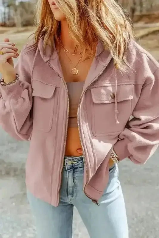 Woman wearing pink zip up hooded jacket with flap pockets and drawstring hood. Casual fall/winter coat styled with jeans and crop top.