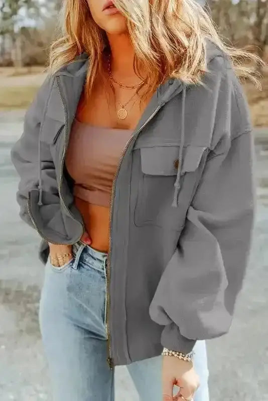Front view of gray zip up hooded jacket for women with flap pockets and drawstring hood, styled for casual streetwear.