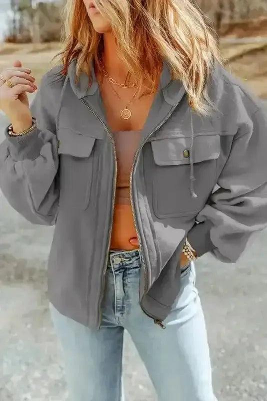 Gray zip up hooded jacket for women styled with jeans, featuring flap pockets and drawstring hood for a casual winter look.