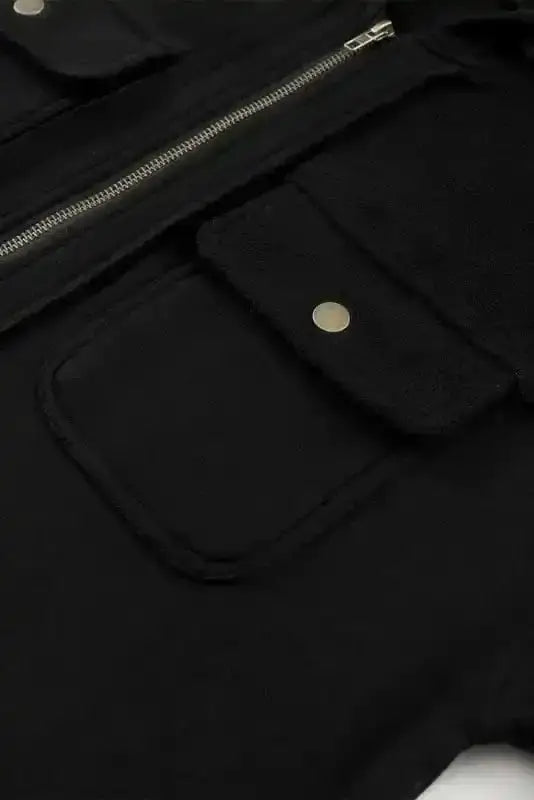 Flap pocket with snap button on black women's hooded jacket, emphasizing functional outerwear design.