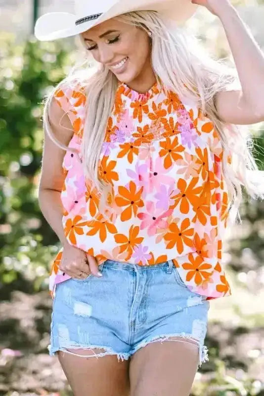 Model smiling in Orange Smocked Floral Top with ruffled sleeves and colorful floral design. Perfect for festivals or warm weather.