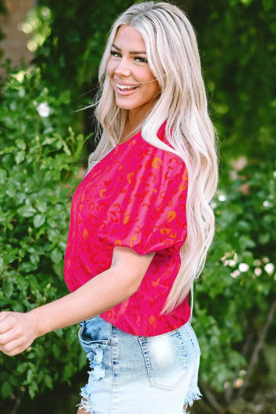 Model posing in a pink leopard print top with denim shorts.