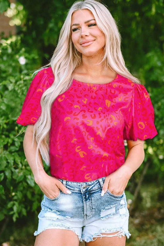 Woman wearing a pink leopard print puff sleeve top with high-waisted jeans, standing outdoors.