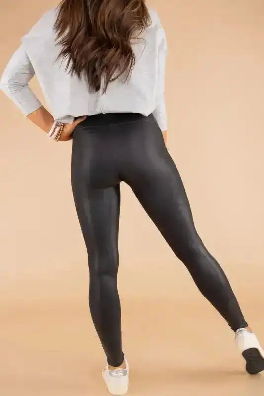 Rear angle of women’s black faux leather skinny leggings, emphasizing stretch fit and glossy PU leather ideal for casual or night looks.