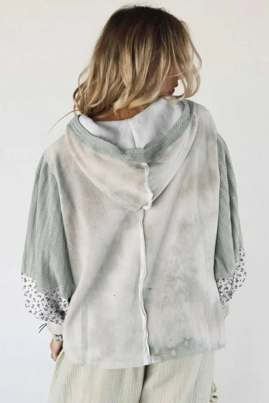Person wearing a light green hoodie with lace sleeves on a plain background