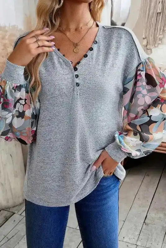 Model wearing Gray Floral-Sleeves Buttoned V-Neck Top with hand in pocket, highlighting playful sleeve print and buttoned neckline.
