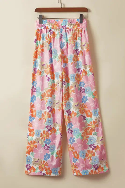 Colorful floral-patterned wide-leg pants with smocked waist hanging on a wooden hanger