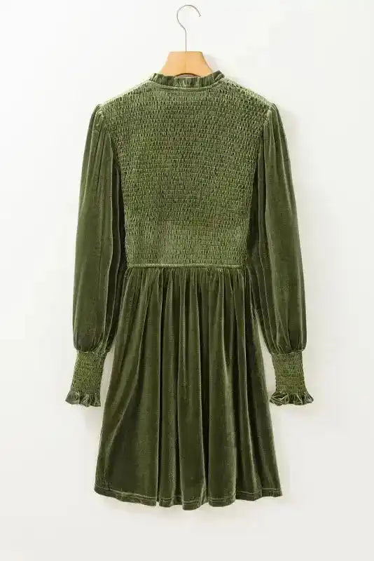 Back view of green velvet dress on hanger, showing smocked bodice and flared skirt, ideal for elegant winter fashion collections.