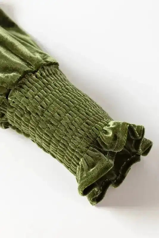 Close-up of smocked velvet sleeve with frilled cuff in green, highlighting the detailed craftsmanship of the dress.