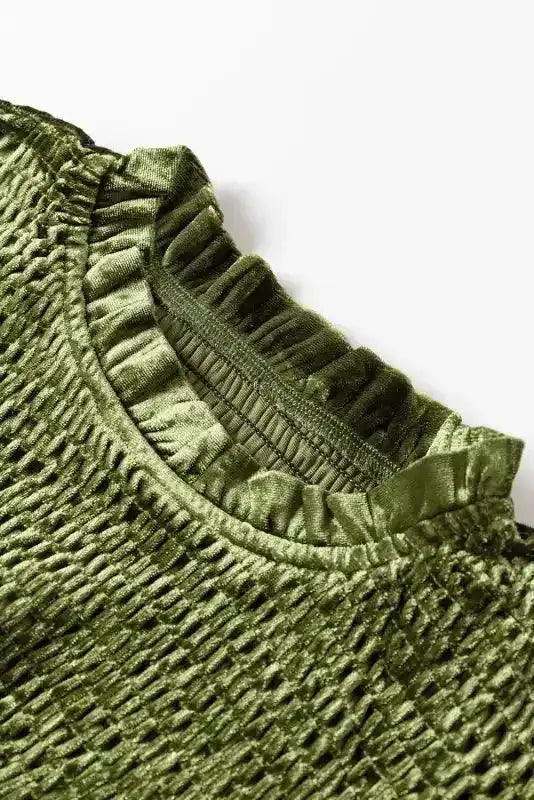 Detailed view of frilled neckline and smocked texture on green velvet dress, emphasizing luxurious fabric and elegant design.