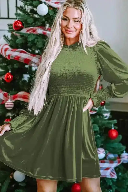 Model wearing green Frilled Neck Smocked Bodice Velvet Dress by FashionFitz, styled for festive winter occasions near a Christmas tree.