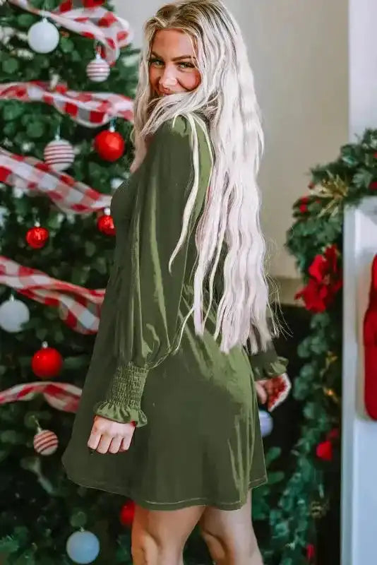 Side profile of model in green velvet dress with smocked bodice and frilled cuffs, styled for a feminine and elegant winter look.