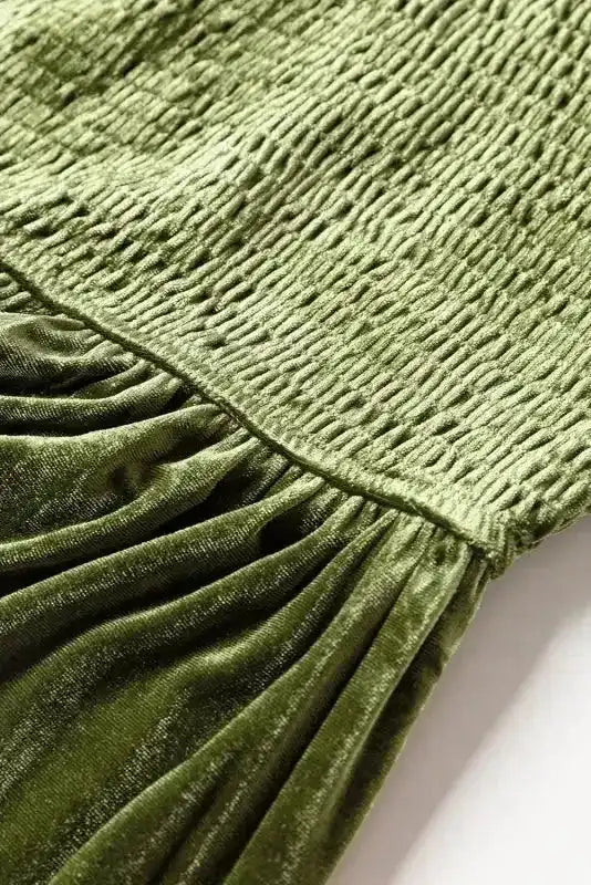 Close-up of smocked bodice and gathered skirt seam on green velvet dress, showcasing fine tailoring and soft texture.